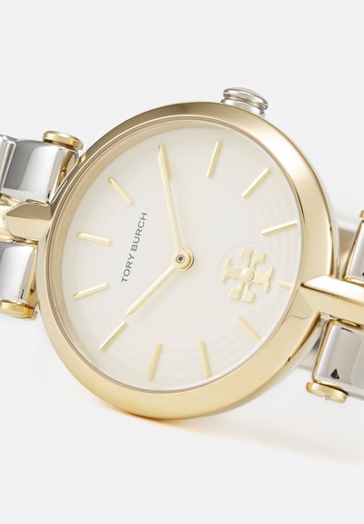 Montre-bracelet Tory Burch en or et argent avec un cadran blanc, des index dorés et sans chiffres, affichant 7h55.
