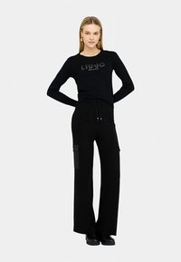 Czarna bluzka z długim rękawem z logo „LIUJO MILANO”, zestawiona z czarnymi szerokimi spodniami z bocznymi kieszeniami i sznurkiem w pasie.
