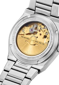 Reloj automático con caja de acero inoxidable, cristal de zafiro y movimiento dorado visible. Presenta detalles grabados y una pulsera metálica.
