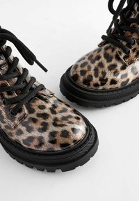 Paire de bottes brillantes à motif léopard avec semelles épaisses noires et lacets noirs sur fond blanc.