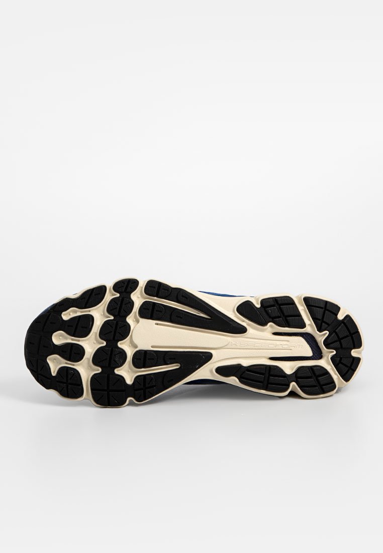 Suela de zapato con una superficie de goma negra texturizada y surcos para tracción, acentuada por una entresuela beige y patrones elevados.