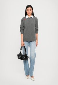 Gray knitted sweater with red heart detail, white collared shirt underneath, light blue floral jeans, black handbag, and cream-colored shoes.