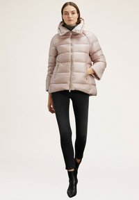Geacă puffer din material roz deschis, cu guler înalt, fermoar frontal și două buzunare laterale. Purtată peste blugi skinny negri și cizme până la gleznă.