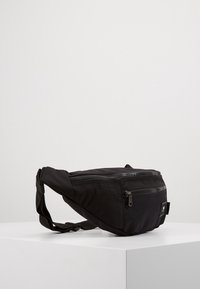 Mustan kankaan vyölaukku, jossa on vetoketjullinen pääosasto, säädettävä olkahihna ja pieni etutasku. Teksturoidun pinnan ja kompakti muotoilu.