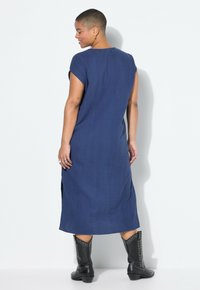 Navyblauwe linnen jurk met korte opgerolde mouwen, zijsplitten en een losse pasvorm. Gerdragen met zwarte gespijkerde enkellaarsjes.