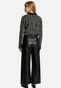 Maglione leopardato nero e grigio con maniche lunghe, abbinato a pantaloni in pelle nera a vita alta e a gamba larga. Orecchini in argento visibili.