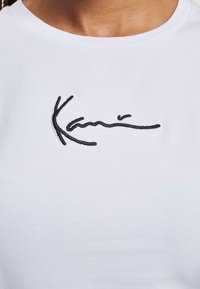 T-shirt bianca in cotone con testo ricamato nero sul davanti. Design classico a girocollo con una texture morbida.