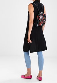 Czarna bezrękawnikowa tunika z rozporkiem po bokach, w zestawie z jasnoniebieskimi, zniszczonymi rurkami, różowymi metalicznymi balerinkami oraz plecakiem w kwiatowy wzór.
