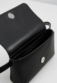 Czarna skórzana torebka o teksturowanej powierzchni, z zamknięciem na srebrny zatrzask i wewnętrznymi przegródkami. Kompaktowy kwadratowy kształt z paskiem na ramię.