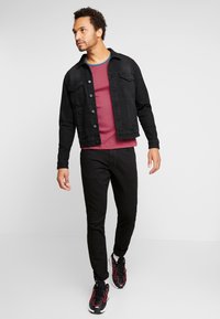 Melna džinsa jaka pār sarkanu un tumši zilu svītrainu kreklu, apvienota ar melniem džinsiem un melnām sporta kurpēm ar sarkaniem akcentiem.