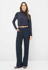 Marineblå turtleneck-top parret med skræddersyede, højtaljede brede bukser, accentueret af et beige bælte. Mønstrede sko fuldender looket.