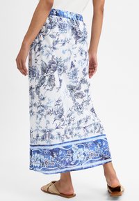 Vloeiende maxi-rok van lichtgewicht stof, versierd met een blauw bloemenpatroon op een witte achtergrond, met een decoratieve blauwe zoom.