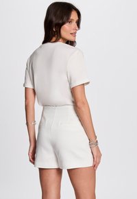 Haut blanc à manches courtes associé à un short blanc taille haute. Le tissu semble lisse, avec des détails subtils aux manches et aux poches.