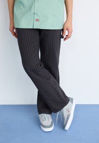 Mintgrön skjorta med knappar, svarta randiga byxor och grå sneakers med orange accenter. Släta, avslappnade texturer och en avslappnad passform.