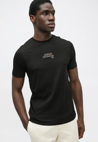 Melna kokvilnas T-krekls ar īsām piedurknēm, ar kontrastējošu izšūtu "Armani Exchange" logo uz krūtīm. Gluda tekstūra un pieguļošs griezums.