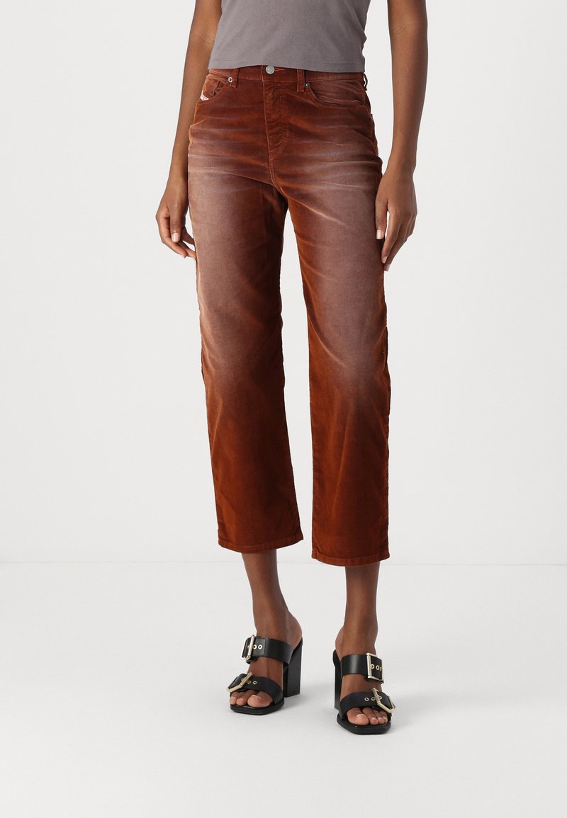 Pantalon corsaire en velours côtelé marron avec un léger éclat, doté de poches avant, passants pour ceinture et coupe droite. Sandales noires à talons avec une boucle.