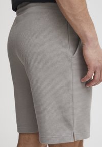 Sive kratke hlače od tkanine s teksturiranim uzorkom, bočnim džepovima i ravnim krojem, s fleksibilnim pojasom i minimalnim detaljima šivanja.
