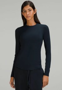 Sort langærmet top med rund udskæring, tekstureret stof og tætsiddende design, båret med matchende mørke bukser. Glat overflade og minimale syninger.