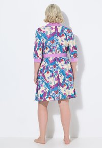 Vestido floral hasta la rodilla en color crema con estampados azules y rosas, con mangas 3/4 y un cinturón morado en la cintura. Textura de tela suave.