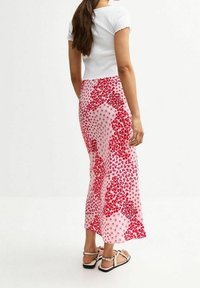 Valkoinen ribatty lyhythihainen toppi vaaleanpunaisista, kukkakuosisista maksihameista, joissa on erilaisia punaisia sävyjä ja tiukka vyötärö.