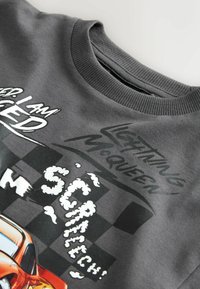 Šedá mikina s designem "Blesk McQueen", pohádkového auta, a textovými prvky v bílé a černé barvě, včetně obláčkových akcentů.