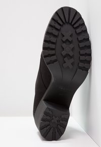 Svart skosula med texturerad gummi för grepp. Har en rundad form och platt klack. Logotyp synlig på sidan, storlek märkt som 37.