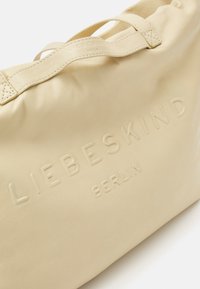 Beżowa torba tote ze skóry z wytłoczonym logo "LIEBESKIND BERLIN", charakteryzująca się gładką teksturą, zwiniętymi uchwytami i minimalistycznym designem.