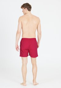 Röda badshorts med elastisk midja, tillverkade av lättviktigt material, knä-långa, med en mjuk textur och inga synliga mönster.