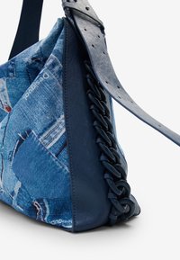 Niebieska torba na ramię wykonana z materiału przypominającego dżins, z teksturowanymi skórzanymi akcentami, plecionymi detalami i płaskim paskiem na ramię.