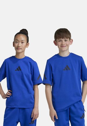 T-shirts de sport bleus en tissu doux, avec le logo noir d'Adidas sur la poitrine et les manches. Portés par une fille et un garçon.