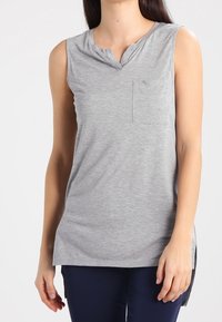 Bezramenné šedé tričko vyrobené z měkké látky, s výstřihem do V, malou náprsní kapsou a uvolněným střihem se bočními rozparky pro snadný pohyb.