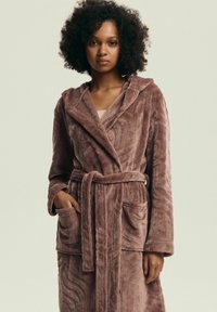 Hooded robe in soft, plush fabric, featuring a textured wave pattern, long sleeves, two front pockets, and a matching belt in mauve.