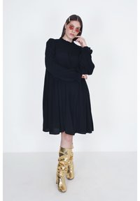 Zwarte lange mouw jurk met tekstuur op het lijfje, vloeiende silhouet en knielengte. Gecombineerd met metallic gouden kniehoge laarzen.