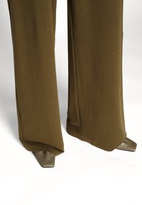 Olivgrön vida byxor tillverkade av mjukt tyg med en slät yta, i kombination med spetsiga, glänsande gråbruna skor.