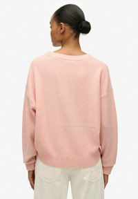 Rosa Pullover mit lockerer Passform, gerippten Bündchen und Saum sowie einem weiten Ausschnitt. Weiche Textur; getragen mit hellen, hochgekrempelten Hosen.