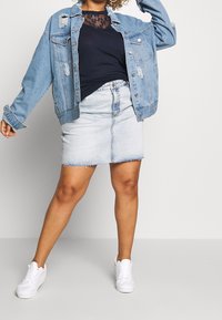 Jeansjacka med slitna detaljer, marinblå skjorta med spetsdetaljer, ljus jeanskjol med fransad nederkant och vita sneakers.