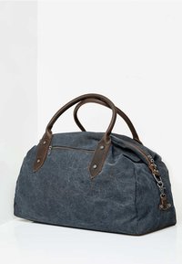 Torba duffel z płótna w ciemnoszarym kolorze z brązowymi skórzanymi akcentami, podwójnymi uchwytami, boczną kieszenią na zamek błyskawiczny oraz teksturowaną powierzchnią.