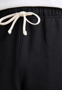Black joggers featuring an elastic waistband with a cream-colored drawstring tie and smooth texture, focused on comfort and minimal design.