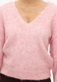 Pull rose tricoté avec un col en V, fabriqué dans un tissu duveteux et doux. Présente une coupe ample et un ourlet côtelé. Aucun motif ou accessoire visible.
