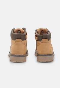 Stivaletti alla caviglia in pelle beige con dettagli marroni, colletto imbottito, cerniere e suole testurizzate. Presentano cuciture rinforzate e materiali resistenti.