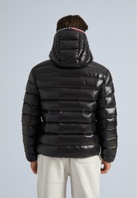 Jachetă puff black cu glugă, textură lucioasă, quilt-ing orizontal și detalii contrastante la gât.