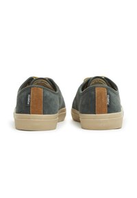 Sneakers verde in suede con suole in gomma beige. Presentano un accento in pelle marrone sul tallone e un'etichetta del marchio sul lato.