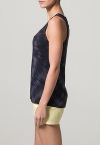 Námořnická modrá tie-dye bezramínková tílko s volným střihem, v kombinaci se světle žlutými šortkami. Tkanina se zdá být jemná a lehká.