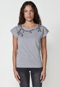 Grå bomullst-shirt med korta ärmar, blommiga utsmyckningar vid halsringningen i mörka pärlor, och en figurnära design.