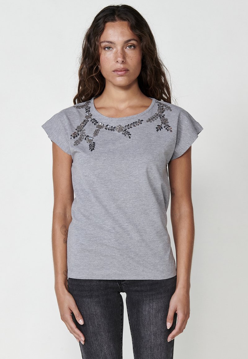 Grå bomullst-shirt med korta ärmar, blommiga utsmyckningar vid halsringningen i mörka pärlor, och en figurnära design.