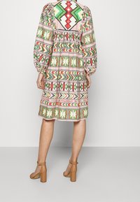 Kleurrijke jurk met een patroon in groene, rode en roze geometrische ontwerpen, ballonmouwen en een losse pasvorm, gecombineerd met beige blokhak sandalen.