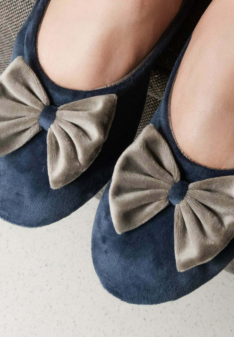 Ballerines bleu marine en suede doux avec de grands nœuds en peluche grise à l'avant. Bout arrondi et texture lisse.