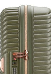 Maleta rígida verde con textura de surcos verticales, cremallera de color rosa dorado y tiradores de doble cremallera, cerradura aprobada por la TSA y acento de marca.