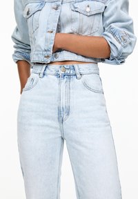 Veste courte en denim bleu clair avec boutons et deux poches poitrine, associée à un jean taille haute bleu clair avec coutures avant.