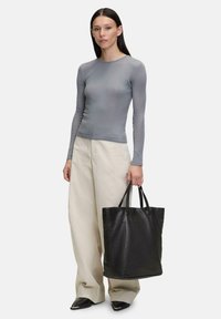 Haut à manches longues gris côtelé associé à un pantalon large crème ; tenant un sac fourre-tout en cuir noir. Textures lisses avec un design structuré.
